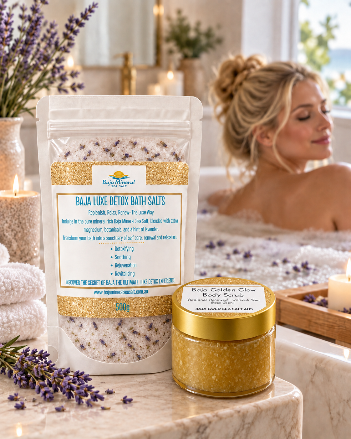 Two bags of Bath Natural bath salts displayed on a marble counter in a spa-like bathroom setting with a woman relaxing in the background. The products include 'Baja Luxe Detox Bath Salts' in a large stand-up pouch and 'Baja Golden Glow Body Scrubs' in a small glass jar with a gold lid.