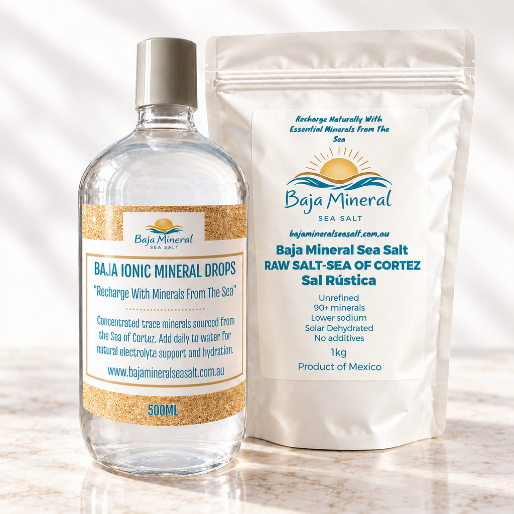 A 500ml bottle of Baja Mineral Ionic Mineral Drops next to a white stand-up pouch of Baja Mineral Sea Salt, both featuring blue and gold labels, set against a bright white background with soft leaf shadows.