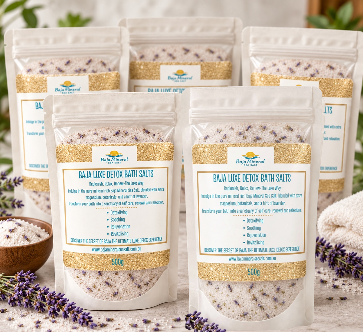 Four stand-up pouches of Baja Luxe Detox Bath Salts arranged in a cluster on a white surface with decorative lavender sprigs at the base. The front pouch is fully visible, with three additional pouches behind it at different angles.