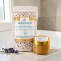 Baja Luxe Detox Bath Salts in a resealable stand-up pouch next to a small jar of Baja Golden Glow Body Scrub, both from Baja Natural, on a marble countertop with lavender sprigs.